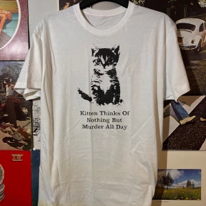 Vit t-shirt med kattmotiv - Säljer en vit t-shirt med ett tryck av en söt katt och texten 'Kitten Thinks Of Nothing But Murder All Day'. Perfekt för dig med humor och kärlek för katter. Passar bra till vardags eller som en rolig present!