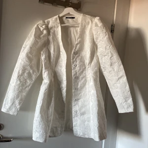 Vit klänning från Gina Tricot🤍 - Säljer en elegant vit klänning från Gina Tricot i storlek 38. Den har ett vackert blommönster och långa ärmar. Perfekt för vår och sommar, med en stilren design som passar både till vardags och fest.  framtill för en klassisk look.🤍