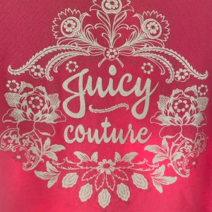 Rosa t-shirt från Juicy Couture - Säljer en superfin rosa t-shirt från Juicy Couture med ett snyggt vitt blommönster och logga på framsidan. Den är kortärmad och perfekt för sommardagar. Gjord i mjukt material för en bekväm passform. Passar perfekt till jeans eller kjol!