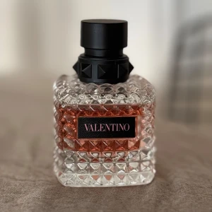 Valentino parfymflaska 50ml - Säljer en lyxig parfymflaska från Valentino. Flaskan är fyrkantig med ett elegant mönster och har en svart kork. Den genomskinliga glasdesignen visar den rosa vätskan inuti. Perfekt för att ge en touch av glamour till din parfymkollektion!