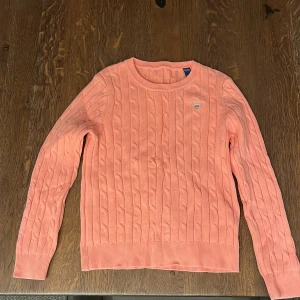 Rosa stickad tröja från GANT, 134/140 - Säljer en superfin rosa stickad tröja från GANT. Den har ett klassiskt kabelstickat mönster och en liten broderad logga på bröstet. Perfekt för både vår och höst! Tröjan är i mycket bra skick och passar perfekt för en stilren look. 🌸