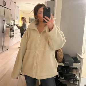Beige teddyjacka med dragkedja - Mysig och varm beige/vit teddyjacka perfekt för kyliga dagar. Jackan har en dragkedja framtill och långa ärmar. Den är i en loose passform vilket gör den superbekväm att bära. Perfekt för höst och vinter! Från Carin Wester! Man kan även dra åt jackan nertill. Pris kan diskuteras. Säljer pga att jag tycker den ser för lång ut på mig. För referens är jag 158