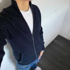 Mörkblå stickad kofta - Säljer en snygg mörkblå stickad kofta. Den har en dragkedja framtill och är perfekt för kyliga dagar. Koftan är i bra skick och passar både till vardags och lite finare tillfällen. Perfekt för höst och vinter!