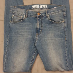 Blå jeans från Sweet SKTBS - Säljer ett par snygga blå jeans från Sweet SKTBS i storlek 31/32. De är i bra skick och har en klassisk femficksdesign med knapp och dragkedja. Materialet är 98,5% bomull och 1,5% elastan, vilket ger en skön passform. Perfekta för vardagsbruk eller en avslappnad utekväll.