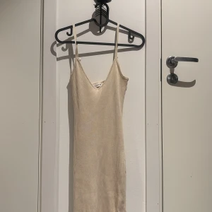 Beige ribbad klänning - Säljer en superfin beige ribbad klänning med smala axelband och v-ringning. Den har en slits på sidan som ger en snygg detalj. Perfekt för sommardagar eller en avslappnad kvällslook. Passar bra med både sneakers och sandaler!