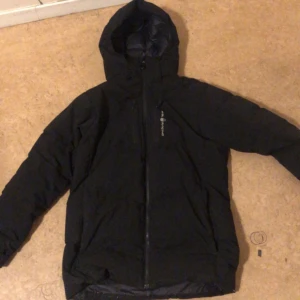 Svart dunjacka från Bergans - Säljer en svart dunjacka från Bergans i bra skick. Den är perfekt för kalla vinterdagar med sin varma och isolerande design. Jackan har en praktisk huva och dragkedja framtill. Passar både till vardags och utomhusaktiviteter. Perfekt för dig som vill hålla värmen i stil! 🖤