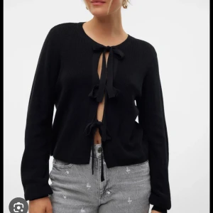 Svart kofta från Vero Moda - Säljer en snygg svart kofta från Vero Moda i storlek M. Den har en unik knytning framtill som ger en extra touch. Perfekt för både vardag och fest! Koftan är i nytt skick med prislappen kvar. Passar perfekt till höst och vinter.