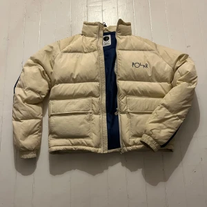Beige/vit pufferjacka från Polar Skate Co. - Säljer en snygg beige pufferjacka från Polar Skate Co. med mörkblå detaljer. Jackan har en dragkedja framtill och är perfekt för kyliga dagar. Den är i bra skick, pris kan diskuteras✅