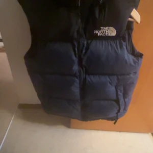 Svart dunväst från The North Face - Säljer en svart dunväst från The North Face i mycket bra skick. Västen har en dragkedja framtill och är perfekt för kyliga höst- och vinterdagar. Den är både stilren och funktionell, idealisk för lager-på-lager-stil. Storleken är M, köpt i mars och hunnit använda den en gång. Har likadan väst i röd om man är intresserad av den istället 