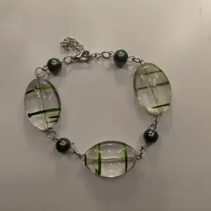 Unikt armband med stora, ovala klara stenar som har gröna linjer inuti. Mellan stenarna finns mörkgröna pärlor. Armbandet har en silverfärgad kedja som är justerbar, för att passa olika handleder. Det är handgjort av mig och superfint för att få en liten färgglad touch i sin outfit !