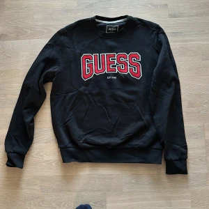 Svart sweatshirt från Guess - Säljer en svart sweatshirt från Guess i bra skick. Den har ett stort rött och vitt Guess-tryck på bröstet. Skön och stilren. Strlk S