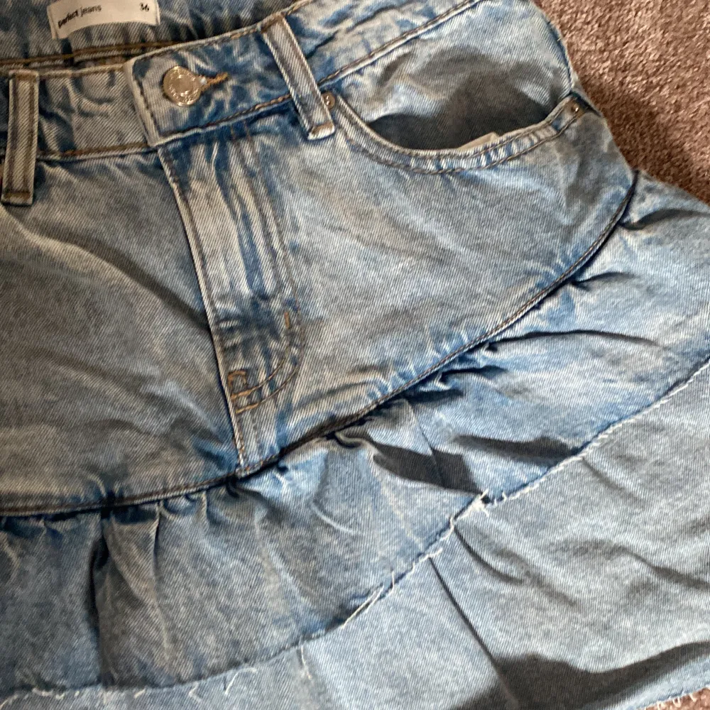 Säljer en superfin jeanskjol från Gina Tricot i storlek 36/S Kjolen är i en härlig blå denim med volangdetaljer som ger en söt look. Perfekt för sommardagar eller en snygg våroutfit. Den har en klassisk jeansknapp och dragkedja framtill. Endast provad så den är som ny! Hör av er vid intresse!💕💕. Kjolar.