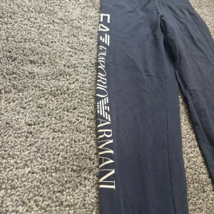 Blå mjukisbyxor från Emporio Armani - Säljer ett par snygga blå mjukisbyxor från Emporio Armani. De har en elastisk midja och loggan tryckt längs benet. Perfekta för en avslappnad stil eller träning. Byxorna är i bra skick och superbekväma!