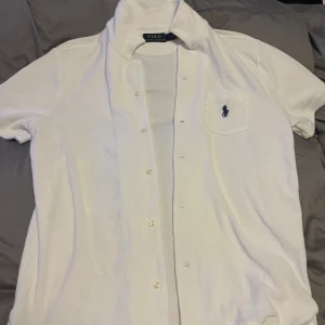 Vit kortärmad skjorta från Polo Ralph Lauren - Säljer en klassisk vit kortärmad skjorta från Polo Ralph Lauren. Skjortan har en stilren design med knappar framtill och en broderad logga på bröstfickan. Perfekt för både vardag och fest! 🕺