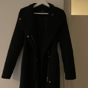 Svart kappa från Vero Moda - Snygg svart kappa från Vero Moda i bra skick. Den har en stilren design med långa ärmar och en dragkedja framtill. Perfekt för höst och vår, och funkar lika bra till vardags som till fest. Storlek xs, men passar även om du brukar ha S.