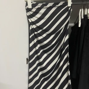 Svartvit randig kjol från H&M - Snygg svartvit randig kjol från H&M i storlek S. Kjolen har en tight passform och är gjord av mjukt och stretchigt material. Perfekt för både vardag och fest! Den har en cool rynkad detalj på sidan som ger en extra touch. 🖤🤍