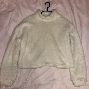 Vit fluffig tröja - Supermysig vit fluffig tröja som är perfekt för kyliga dagar. Den har en hög krage och är croppad, vilket ger en trendig look. Tröjan är långärmad och gjord i ett mjukt material som känns som fleece. Perfekt för höst och vinter!