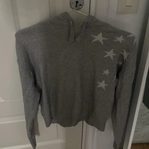 Grå hoodie med stjärnor - Säljer en grå hoodie med coola stjärnor på framsidan och baksidan. Den har en bekväm passform och är perfekt för både höst och vinter. Huvan ger extra mysfaktor och den är i bra skick. Perfekt för en avslappnad stil!
