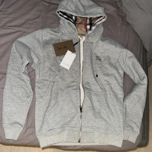Grå hoodie Burberry - Säljer en snygg grå hoodie från Burberry i nytt skick. Det är storlek M men den sitter mer som en S. Oanvänd med tags kvar, perfekt nu till hösten/vintern då den är varm. Skriv för frågor. 1.(1) Har en svart också en för 600 eller båda för 1000.