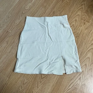 Beige kjol med slits - Säljer en stilren beige kjol i mycket bra skick. Kjolen har en enkel design med en liten slits framtill som ger en snygg detalj. Perfekt för både vardag och festliga tillfällen. Passar bra till både sommar och vår.