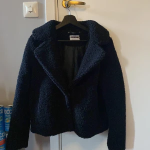 Svart teddyjacka - Mysig svart teddyjacka i bra skick. Perfekt för höst och vinter med sin varma och fluffiga design. Jackan har långa ärmar och en klassisk krage. Den är både stilren och bekväm, idealisk för kyliga dagar. Den ser marinblå ut på bilderna men den är svart!💞💞 hör av er för frågor