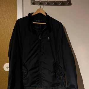 Blå Polo Ralph Lauren Jacka - Säljer en snygg blå  jacka från Polo Ralph Lauren i mycket bra skick. Den har en dragkedja framtill och ett stilrent broderat märke på bröstet. Perfekt för regnigare dagar. Passar både till vardags och lite finare tillfällen Sitter snyggt på mig som är 180cm och väger 70kg