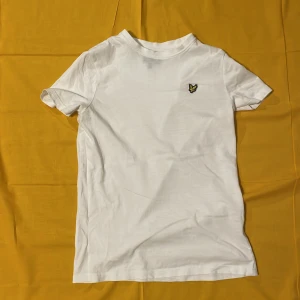 Vit t-shirt med logga - Säljer en vit t-shirt i bomull med en liten logga på bröstet. Den är kortärmad och har en klassisk rund hals. Perfekt för sommardagar eller som basplagg i garderoben. Passar till allt och är superbekväm!