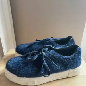 Mörkblå sneakers med pälsdetaljer - Säljer ett par unika mörkblå sneakers med pälsdetaljer. De har en vit sula och snörning framtill. Perfekta för att ge din outfit en cool och annorlunda touch. Använda men i bra skick. 