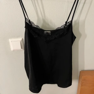 Svart linne från JDY - Säljer ett stilrent svart linne från JDY i storlek 34. Det har tunna axelband och en vacker spetsdetalj vid halsringningen. Perfekt för både vardag och fest! 🖤