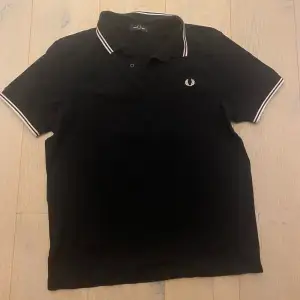 Säljer en klassisk svart pikétröja från Fred Perry i storlek XL. Tröjan har vita detaljer på kragen och ärmsluten samt den ikoniska loggan broderad på bröstet. Perfekt för en stilren och avslappnad look.