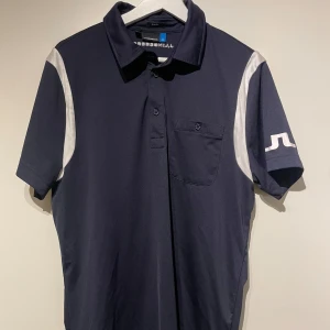 Mörkblå Golfpiké från J.Lindeberg - Säljer en snygg mörkblå golfpiké från J.Lindeberg i slim fit-passform (jag skulle dock säga att den sitter mer som regular). Har en bröstficka samt JL-märket på vänster axel. Perfekt för en runda golf eller andra aktiviteter!
