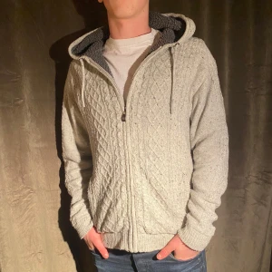 Fodrad Cardigan Jacka - Säljer en supermysig grå stickad cardigan jacka med dragkedja. Den har ett snyggt mönster och är fodrad med mjuk fleece på insidan. Perfekt för kyliga höst- och vinterdagar. Den har långa ärmar och en praktisk huva. Passar både till vardags och chillkvällar hemma.  Vid minsta fråga eller fundering hör av er🤝