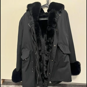 Svart pälsjacka Fatima parka med äkta päls - Säljer en supermysig svart jacka med äkta päls. Den har en stor fluffig luva, pälsen är även avtagbar. Perfekt för kalla vinterdagar när du vill hålla dig varm och stilren. Passar både till vardags och festliga tillfällen. Den är super fin och varm. Använt fåtal gånger! Storlek S