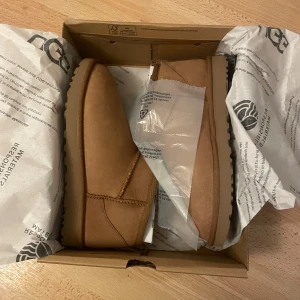 HELT NYA Classic Ultra Mini uggs - Säljer ett par helt nya bruna UGG boots som aldrig har använts och är i original förpackning. Behöver tyvärr sälja dem eftersom de var i fel storlek 💔De är gjorda i mjukt skinn och har en bekväm passform. Perfekta för höst och vinter med sin varma och mysiga insida. Skorna är i storlek dam 38 och har en klassisk design som passar till det mesta. 2150kr originalpris. 