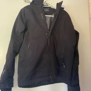 Svart jacka från Vertical - Säljer en svart jacka från Vertical i bra skick. Den har en dragkedja framtill och kardborreband för extra skydd. Jackan är perfekt för höst och vinter med sitt vattentäta material (W-PRO 15000). Den har långa ärmar och flera praktiska fickor. Perfekt för utomhusaktiviteter!