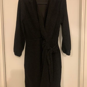 Svart glittrig klänning med knytband - Snygg svart glittrig klänning i medium storlek. Den har långa ärmar och ett knytband i midjan för en fin passform. Perfekt för festliga tillfällen när du vill glänsa lite extra! ✨