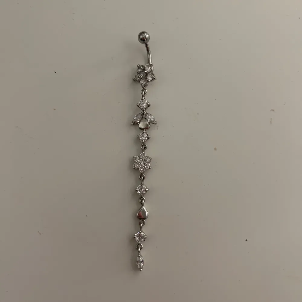 Säljer en superfin silverfärgad navelpiercing med flera glittrande strassstenar i olika former. Perfekt för att ge lite extra bling till din look! Piercingen har en böjd stav och en kula för enkel fastsättning. Passar perfekt till fest eller vardag.. Accessoarer.