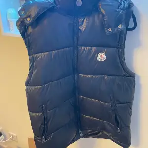 Säljer en snygg svart dunväst från Moncler i mycket bra skick. Västen har en dragkedja framtill och två praktiska fickor med dragkedjor. Perfekt för höst och vinter när du vill hålla dig varm och stilren. Passar både till vardags och lite finare tillfällen.