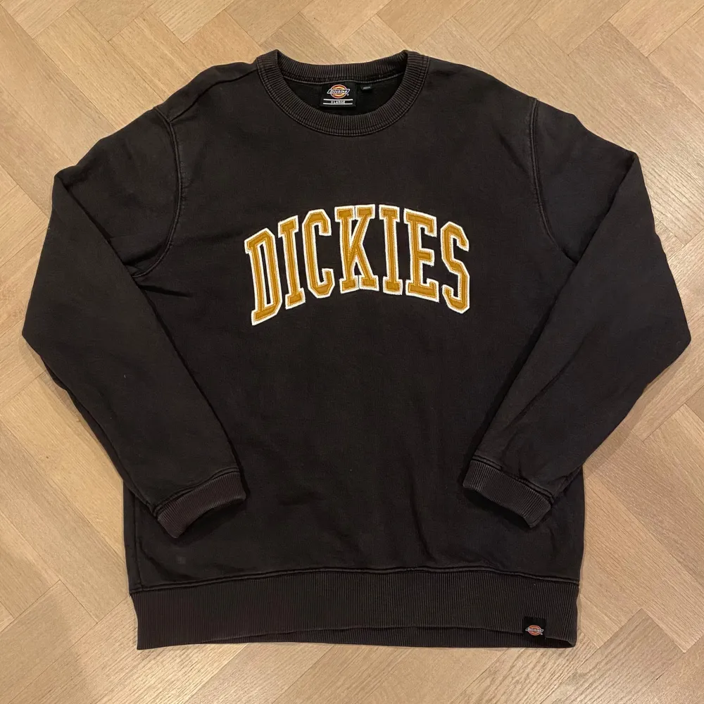 Säljer en svart sweatshirt från Dickies i storlek XL. Tröjan har ett stort gult och vitt tryck med märkesnamnet på framsidan. Den är i bra skick och perfekt för både höst och vinter. Passar till en casual stil och är superbekväm att ha på sig. Perfekt för dig som gillar streetwear!. Tröjor & Koftor.