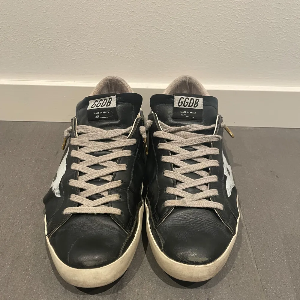 Säljer ett par svarta Golden Goose sneakers.. Perfekta för en avslappnad och trendig stil. Kommer med originalkartong. Skorna har en liten reva på sidan men som är lätt att laga. Där av det låga priset.. Skor.