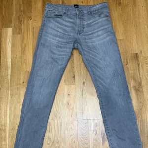 Grå jeans från Hugo Boss - Säljer ett par snygga grå jeans från Hugo Boss i mycket bra skick. De har en klassisk femficksdesign och är perfekta för både vardag och fest. Jeansen har en normal passform (Rugular) och är tillverkade i ett bekvämt denimtyg. Perfekta för höst och vår!