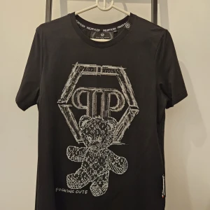 Svart t-shirt från Philipp Plein - Säljer en svart t-shirt från Philipp Plein med ett coolt nalletryck och texten 'Fucking Cute' på framsidan. T-shirten är i bomull och har en normal passform. Perfekt för en avslappnad stil!