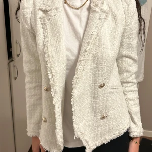 Vit kavaj med guld knappar  - Säljer en superfin vit kavaj. Den har en klassisk look med knappar framtill och är perfekt för både vardag och fest. Kavajen är i bra skick och har en normal passform. Perfekt för att ge din outfit en stilren touch!