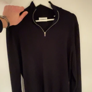 Svart tröja från J.Lindberg - Säljer en stilren svart tröja från J.Lindberg. En 1/4 zip tröja, perfekt för både vardag och fest. Tröjan är i mycket bra skick och passar till alla tillfällen. Skicka ett meddelande vid intresse! Priset är inte hugg i sten