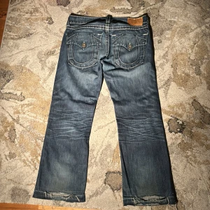 Ovanliga True Religion Fullsize pocket jeans - Ovanliga True Religion jeans strl W32 L32. Det är ett hål vid högra fickan där fram och tecken på slitage där nere men annars är de i bra skick