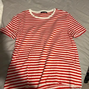 Röd- och vitrandig t-shirt från Zara - Säljer en snygg röd- och vitrandig t-shirt från Zara. Den är kortärmad och har en klassisk rund halsringning. Perfekt för en avslappnad sommarlook eller att bära under en jacka på våren. T-shirten är i bra skick och gjord av mjukt bomullsmaterial.