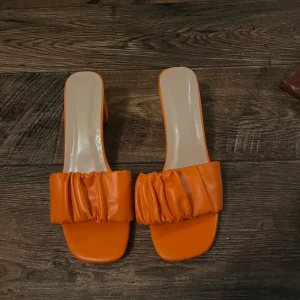Orange sandaler med klack - Snygga orange sandaler med klack och en unik rynkad detalj över foten. Perfekta för sommarens alla tillfällen. De har en öppen tå och en bekväm passform. Perfekt för semester och utomlands 