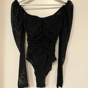 Body med stjärnor - Snygg svart body från Kiss The Sky i storlek XS. Har en tight passform med rynkade detaljer och långa ärmar i mesh. Fina stjärnor över hela bodyn.  Aldrig använd. Perfekt för en utekväll, fest eller nyår! 🖤Skicka gärna prisförslag, går med på det mesta!💕