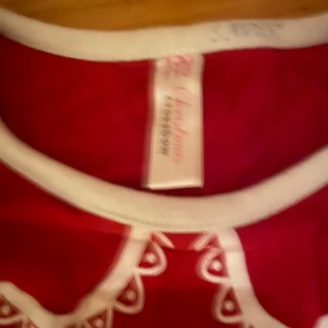 Pepparkaksklänning  - Söt röd klänning med vita detaljer. Den har långa ärmar och ett gulligt mönster med hjärtan och stjärnor. Perfekt för jul eller andra festliga tillfällen. Klänningen har en vit krage och är i bra skick.