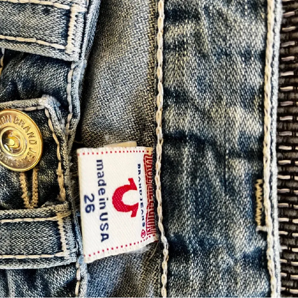 Säljer ett par snygga blå jeans från True Religion i storlek 26. De har en bootcut-stil med slitna detaljer för en cool look. Jeansen är tillverkade i USA och har knappar framtill. Perfekta för en avslappnad stil!. Jeans & Byxor.